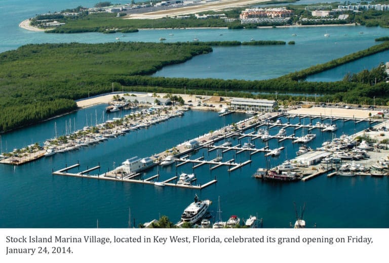 Aerial view of Stock Island Marina Village Key West featuring concrete docks surrounded by clear blue water and boats.