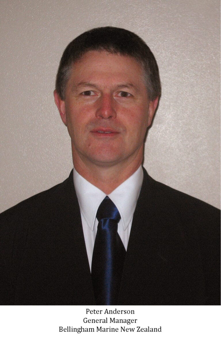 Peter Anderson Bellingham Marine NZ stands smiling in an office setting, wearing a suit and tie, with a window view behind.