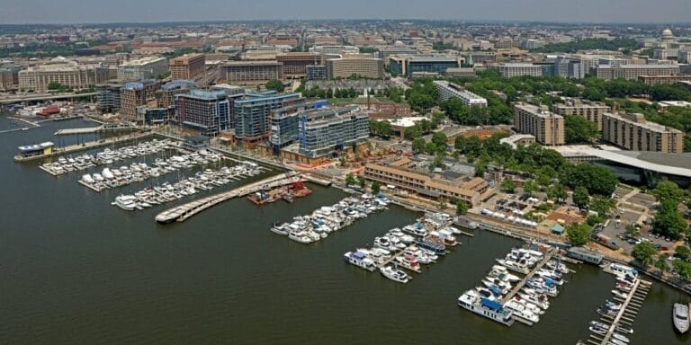 Aerial view of a vibrant urban waterfront revitalization project with modern buildings, green spaces, and docked boats.