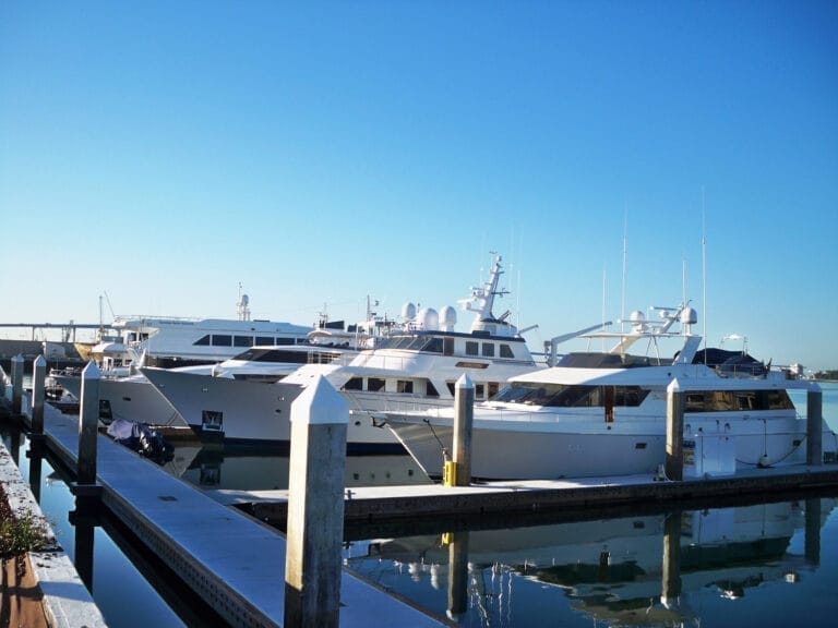 Aerial view of Fifth Avenue Landing marina with yachts docked, surrounded by city buildings and a clear blue sky.