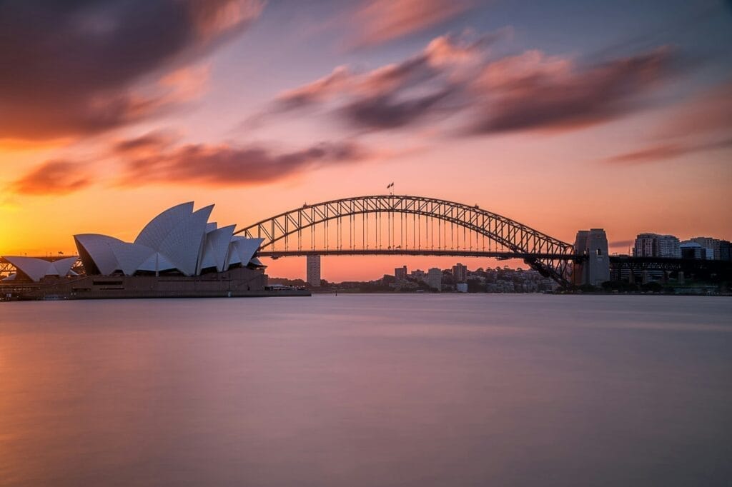 Sydney Harbor Bridge at sunset with light pink and blue sky in the background, capturing the iconic structure's silhouette.