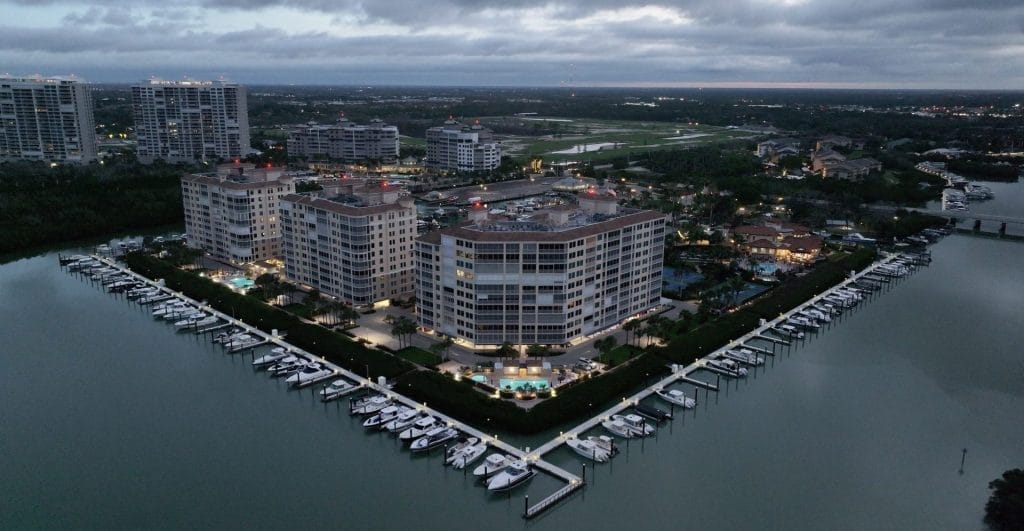 Aerial view of Pelican Isle Yacht Club Marina with boats docked along piers, surrounded by blue water and lush greenery.